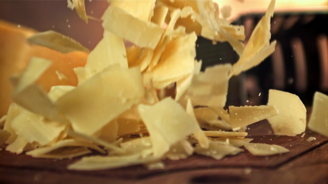 Copeaux de fromage parmesan tombant au ralenti sur une planche en bois
