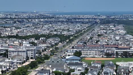 main street leading to stone harbor beach in new jersey. sunny day with blue atlantic ocean in distance. aerial panorama wide shot. traffic scene in american coastal town of usa