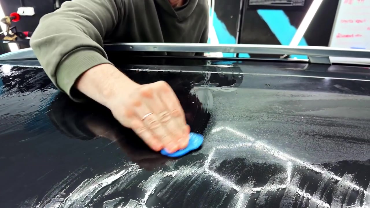 Profissional de detalhamento automotivo realizando correção de pintura através da descontaminação (com clay bar) do teto preto brilhante de um carro.