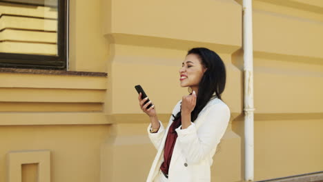 Excited-businesswoman-using-phone-outdoors.-Young-woman-walking-outside