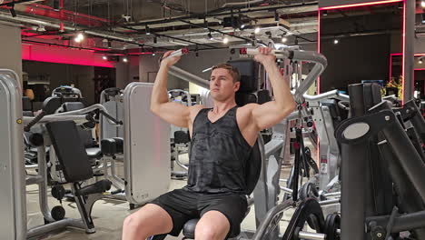 fit man trains shoulders doing shoulder press exercise in machine at modern gym