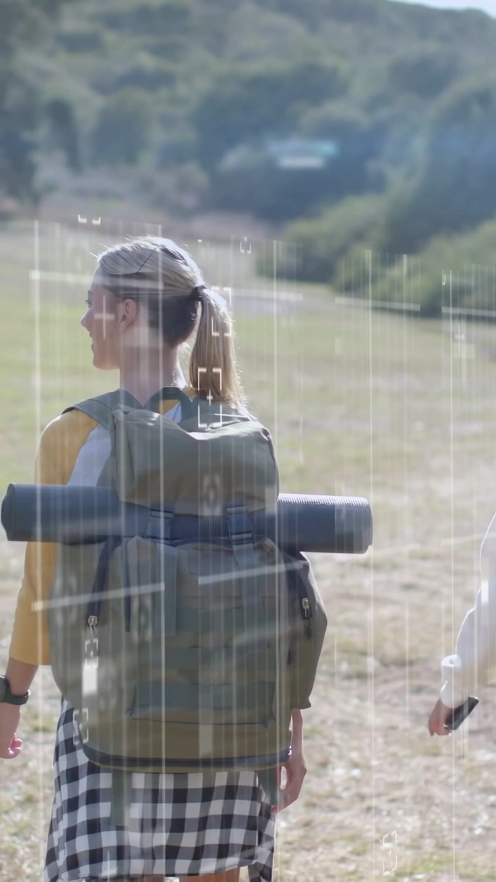 Video verticale: Un escursionista cammina in un campo mentre un amico parla, l'HUD della telecamera monitora lo zaino da viaggio.