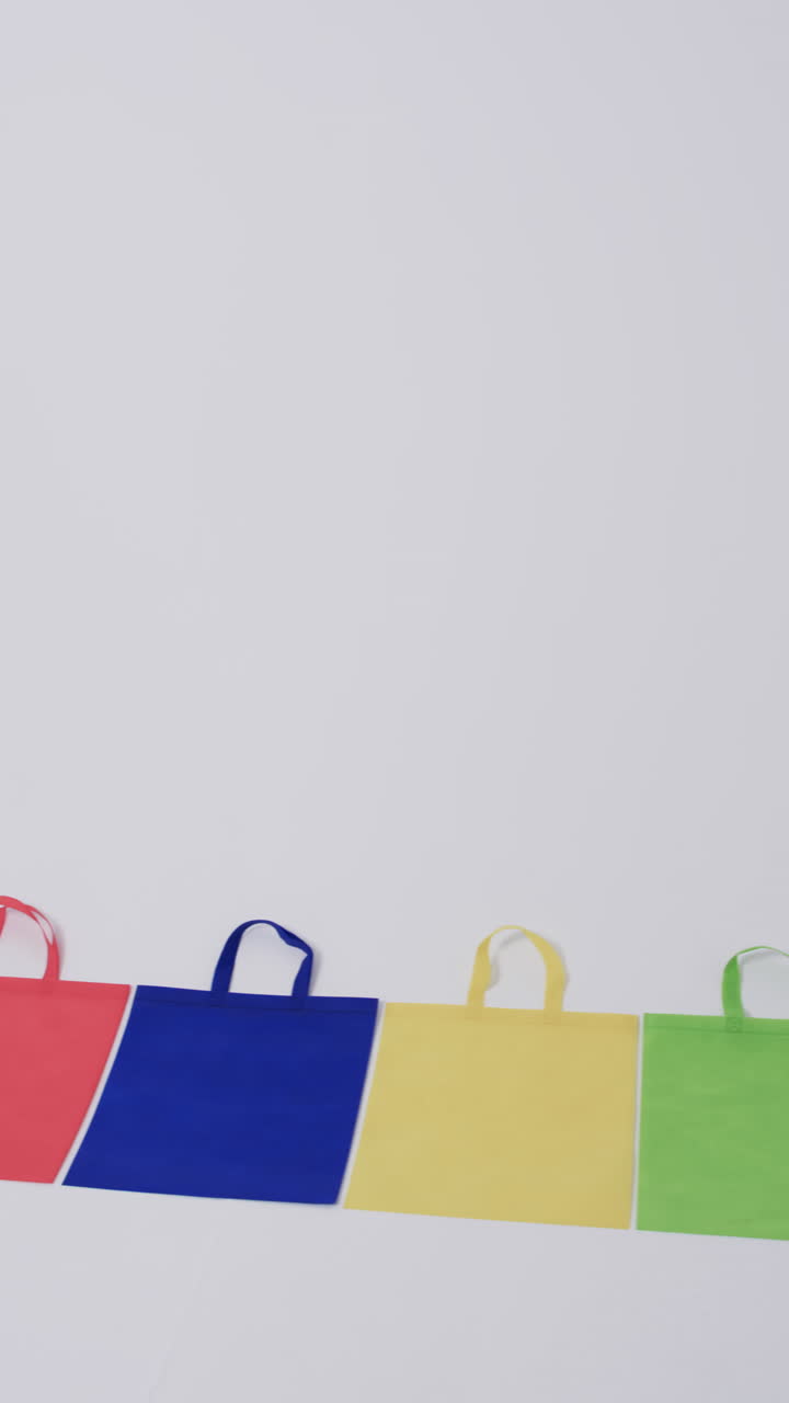 Vertical video of row of multi coloured canvas bags with copy space on white background