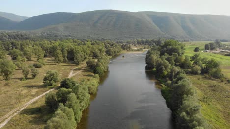 drone video flying over nestos river greece on a sunny day summer , trees on the shore bank left and right , a mountain in the distance