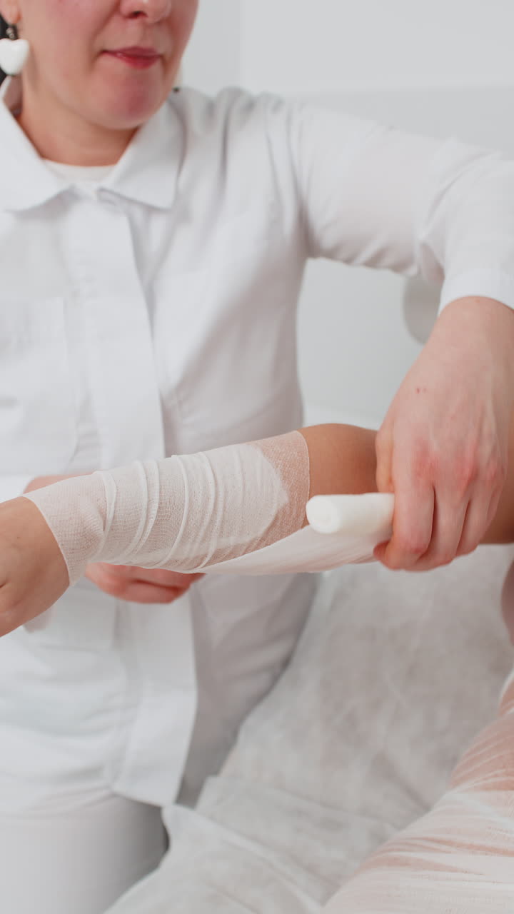 Cosmetologist warping woman hand with compression elastic bandage body mask regeneration weight loss