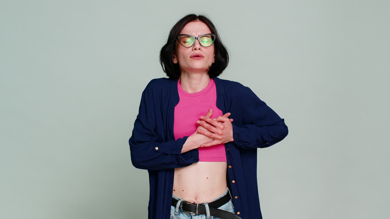 Woman holding chest looking sadly down expressing heart pain emotional grief sorrowful reaction