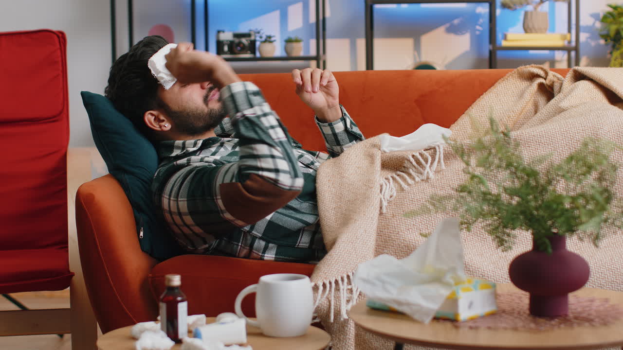 병든 인도인 남자가 감기나 알레르기를 고 집 소파에 누워서 재채기를 하고 킨에 을 니다.