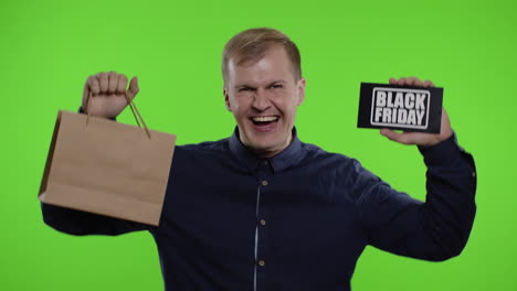 man showing shopping bags and black friday inscription, looking astonished by low cost purchase