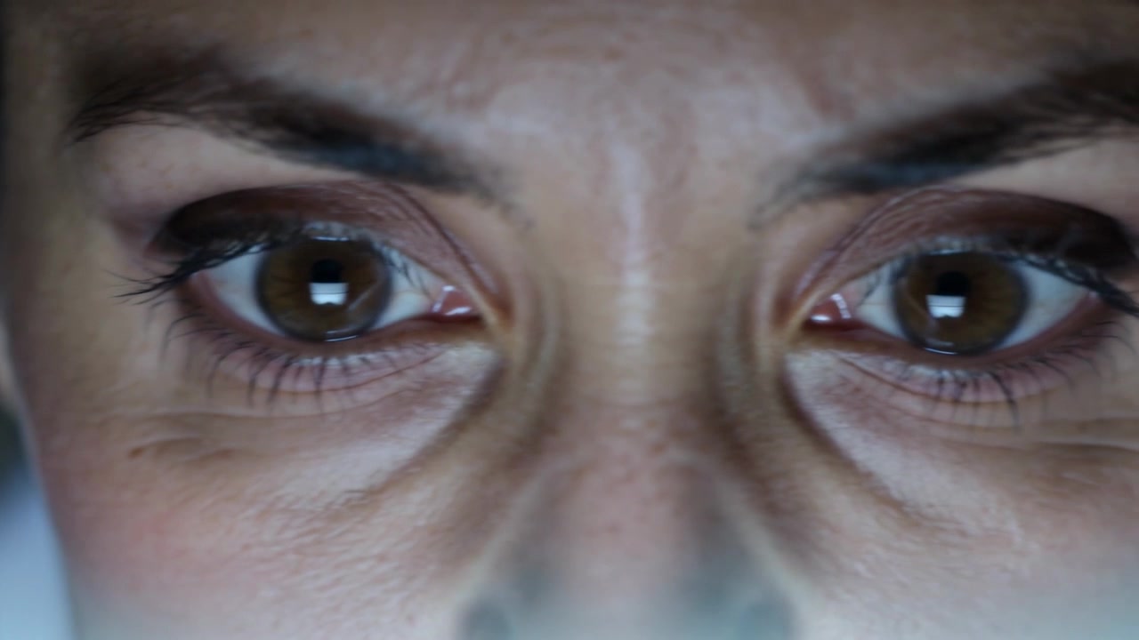 Olhos de mulher piscando reagindo ao reflexo brilhante da tela em close-up, revelando reflexos de lágrimas.