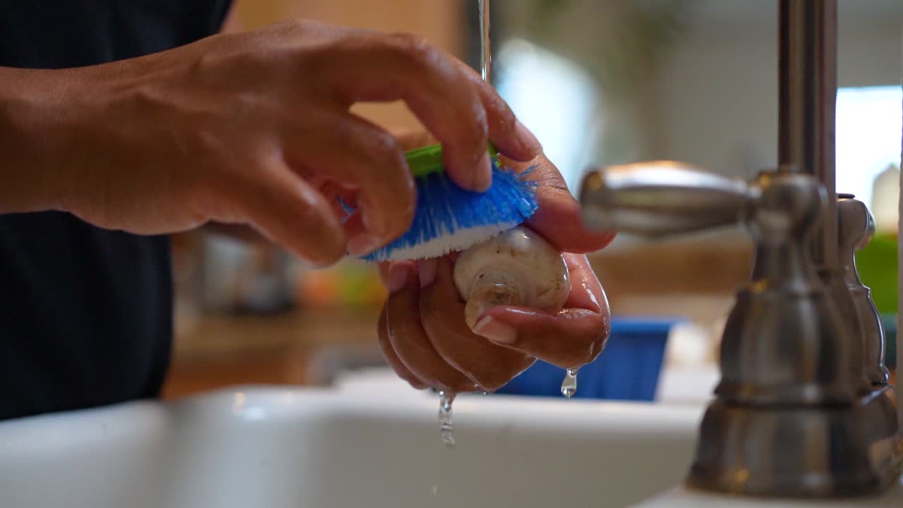 limpieza de setas orgánicas bajo el agua del grifo del fregadero de la cocina en cámara lenta