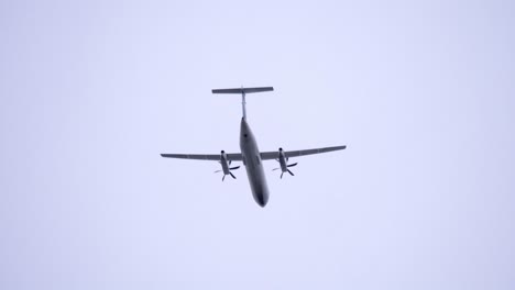 passenger propeller airplane flying overhead, overcast sky background