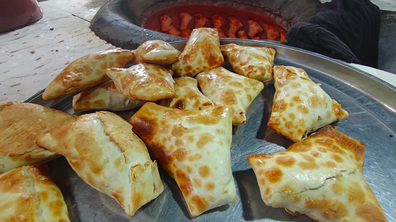 Panadero sacando samsa recién horneado de un horno tandoor tradicional.