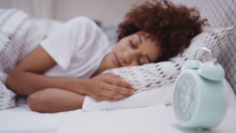 woman asleep in bed reaches out to turn off alarm clock on bedside table