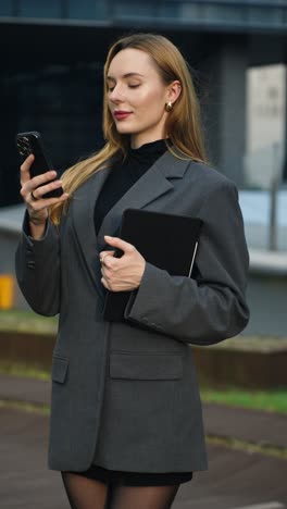 a caucasian professional woman looks at her phone screen while holding a tablet on a seoul rooftop at sunset, filmed in a vertical parallax shot