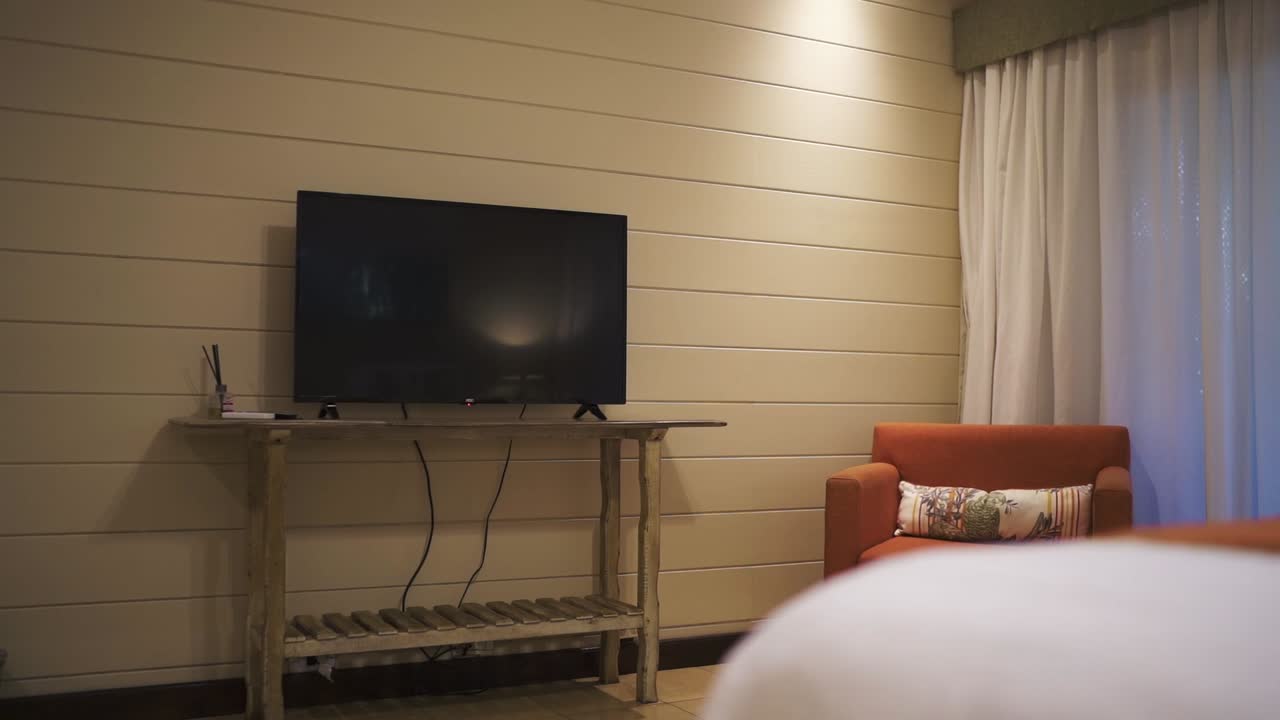 A slow-moving shot reveals a luxurious hotel room with a large flatscreen TV. The elegant interior and modern amenities offer a comfortable and tech-savvy guest experience.