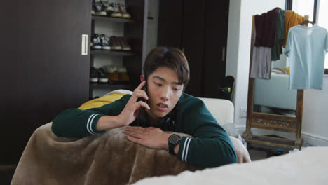 asian boy talking on smartphone lying on the couch at home