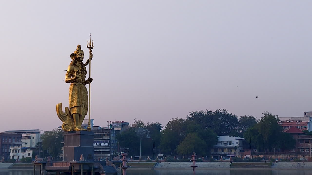 disfruta de una hermosa vista lateral de la inmensa estatua dorada del señor shiva en el lago sursagar, vadodara, a medida que se pone el anochecer, creando una atmósfera serena y encantadora