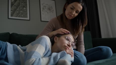 caucasian teenage keeping head on mother's legs while lying on sofa