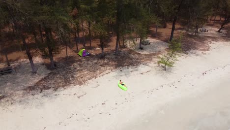 Hombre-Acostado-En-El-Sofá-De-Aire-Verde-En-La-Playa-De-Arena-Con-Carpa-Detrás