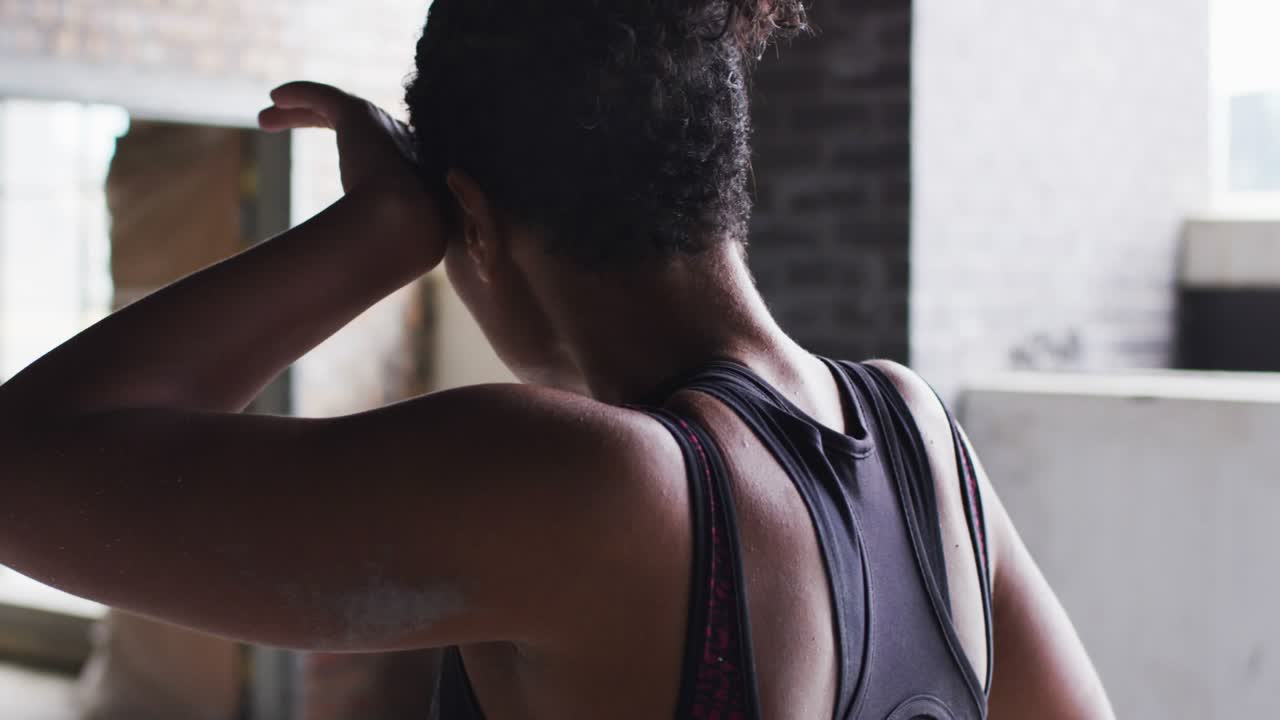 Woman adjusting bun, breathing and recovering in gym while START glitch resolving, revealing face