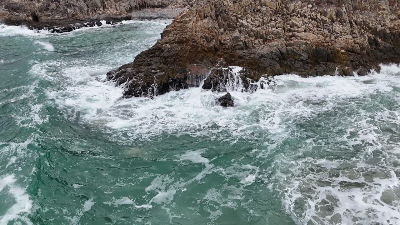 Images de puissantes vagues océaniques s'écrasant sur des rochers noirs, capturant l'écume des vagues, les éclaboussures d'eau et le mouvement côtier énergique pour des projets cinématographiques ou de nature.