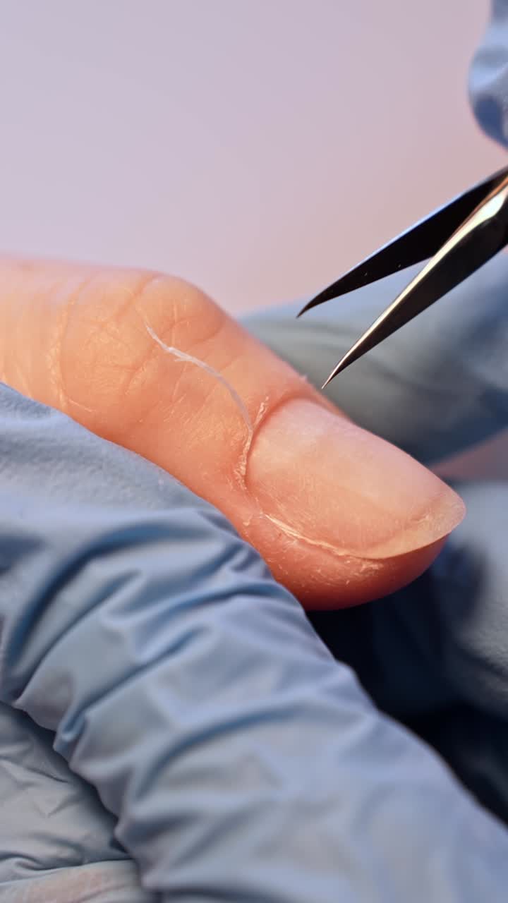 Primo piano estremo di un'onicotecnica che taglia la linea delle cuticole con forbici sottili, mostrando guanti blu, la texture naturale dell'unghia e una preparazione precisa per la manicure da salone.