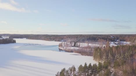 Aerial-over-a-frozen-lake-with-sun-shining-and-green-pine-trees