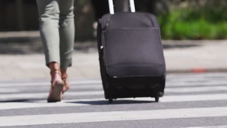 low section of african american woman crossing road wheeling suitcase