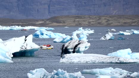 a small touristic boat passes near some huge icebergs