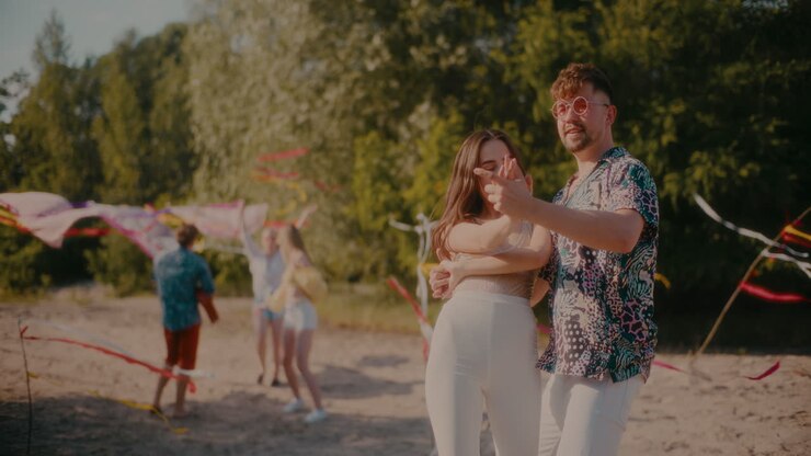 Happy young couple dancing bachata while friends enjoying at beach
