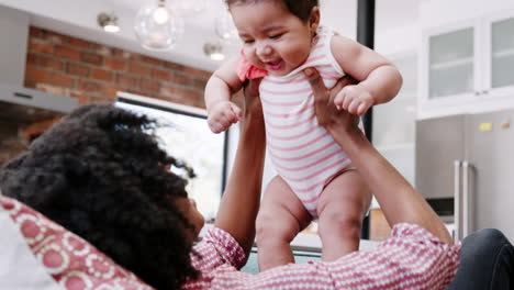 mother lying on sofa and lifting baby daughter into the air