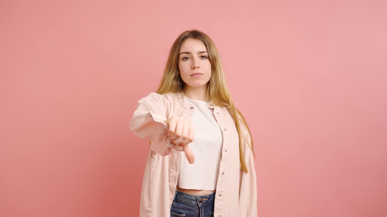 Giovane donna che esprime disapprovazione con il pollice verso il basso su sfondo rosa