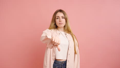 young woman expressing disapproval with thumbs down on pink background