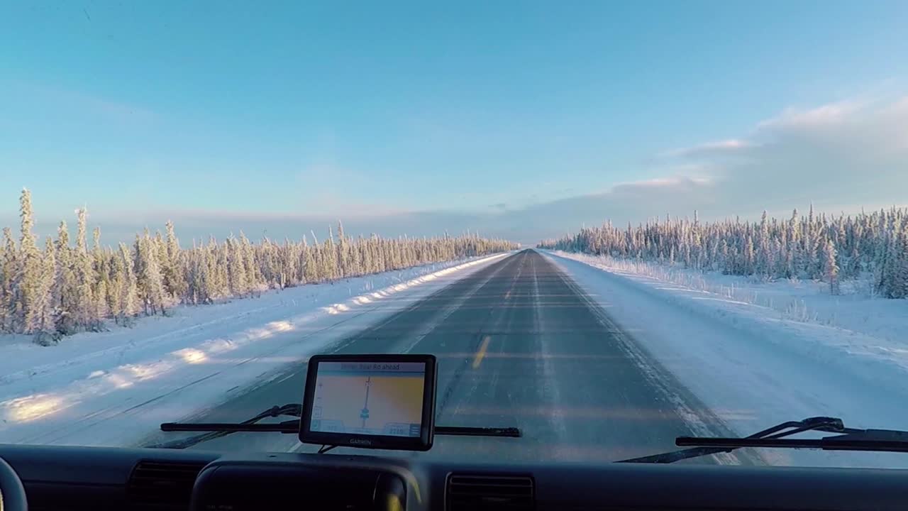 POV shot driving on a arctic road, surrounded by polar forest, GPS on, at golden hour, in Alaska, United States