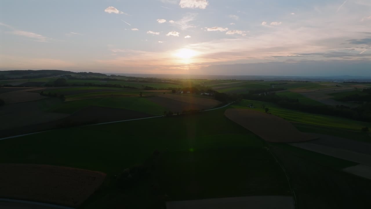 Sunset light casts a warm glow over cultivated fields and green hills in rural Kurnberg, Austria. Aerial dolly in shot