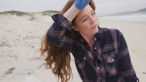 mujer caucásica con guante de látex frotando la frente mirando hacia el mar y sonriendo
