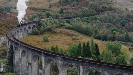 slow circling left of glenfinnan viaduct with steam train crossing in highland landscape