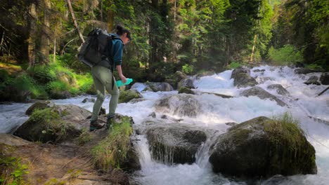 female traveler with a backpack, drinking water in nature in the forest near a mountain river.