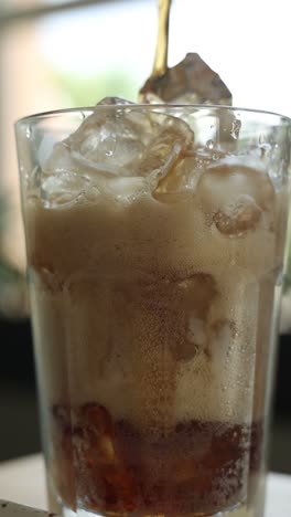 pouring soda into a glass with ice