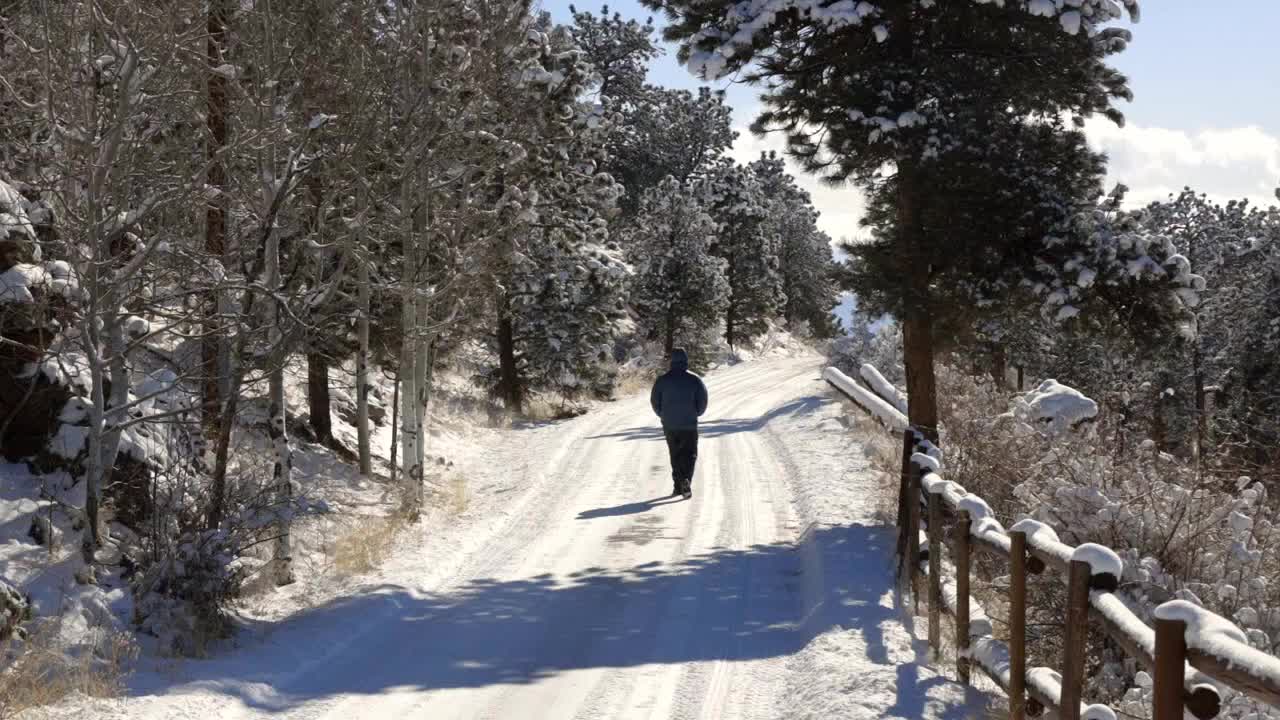 Um homem sozinho caminhando por uma entrada coberta de neve, afastando-se da câmera em direção à distância durante o inverno.