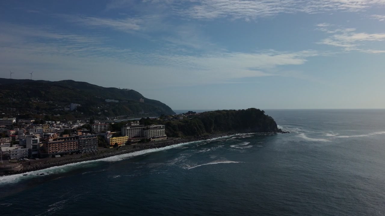 Località balneare costiera con edifici alberghieri sulla collina che si estendono lungo una spiaggia rocciosa curva a Higashiizu, Izu, Giappone, sotto la chiara luce di mezzogiorno, ripresa aerea con drone