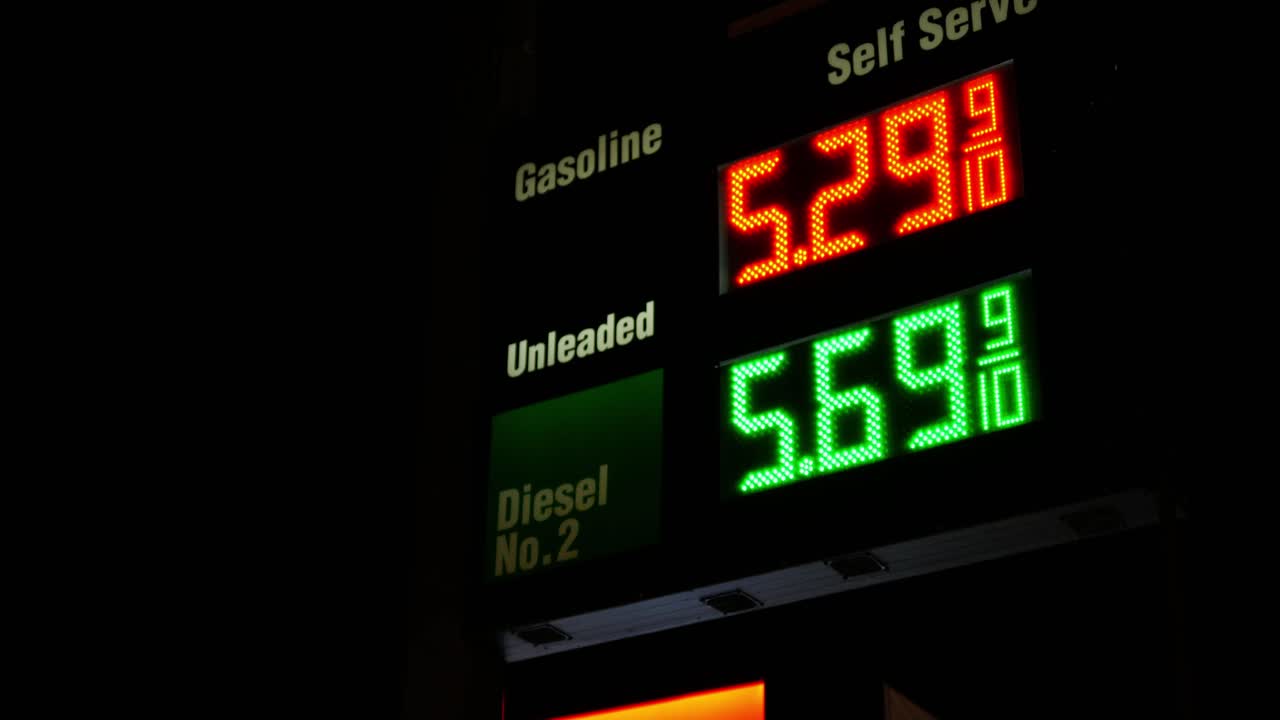Gas station prices LED light up sign for regular and diesel fuel at night over 5 dollars per gallon credit and cash price, during 2021 2022 war time recession, ground up shot zooming out and moving