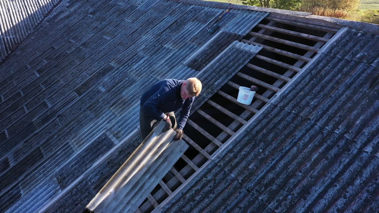 Worker passing an asbestos slate for roof repairs, aerial view