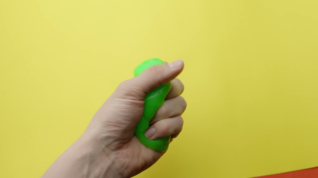 Sticky green slime stretches between Caucasian hands over a vivid yellow backdrop.