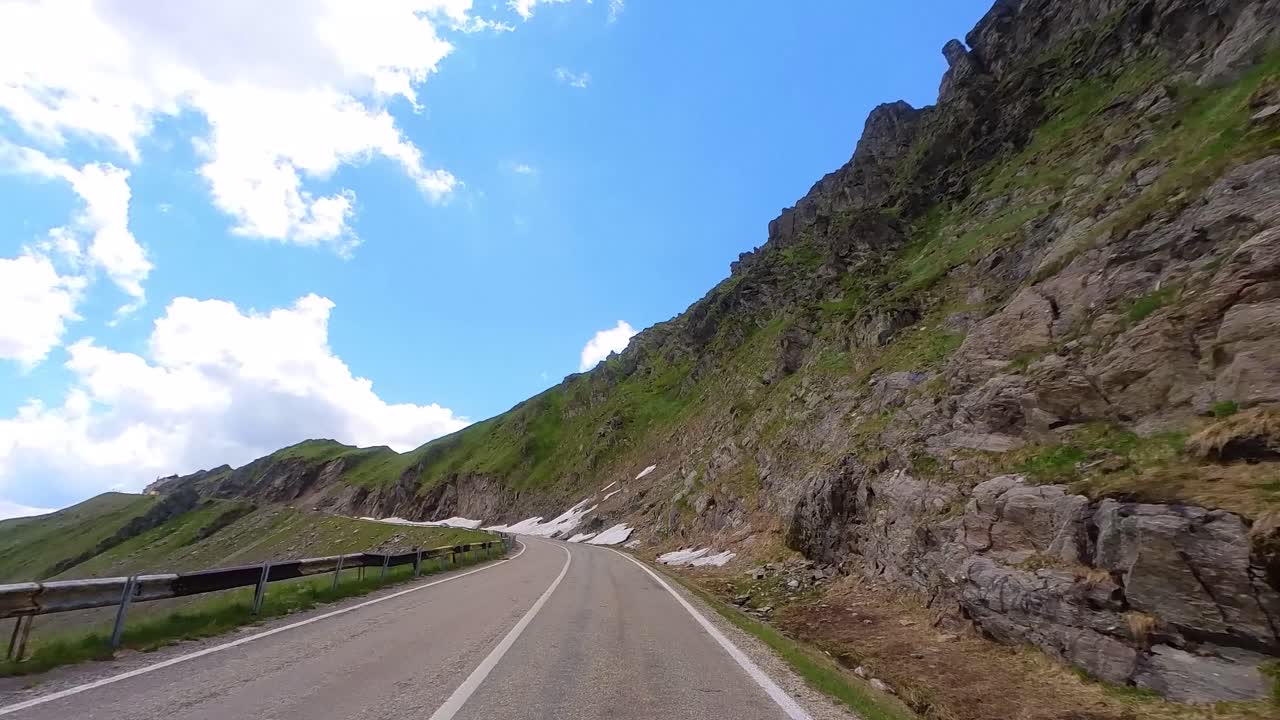 conduzca despacio por un camino de montaña, conductor pov, lado alto de la montaña con manchas de nieve, cielo azul claro, autopista transfagarasan, rumania