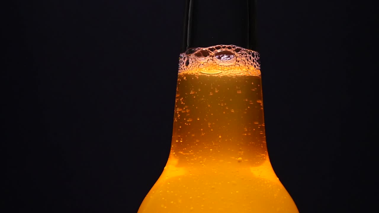 cuello largo retroiluminado botella fría y fresca de cerveza ámbar con burbujas en aumento