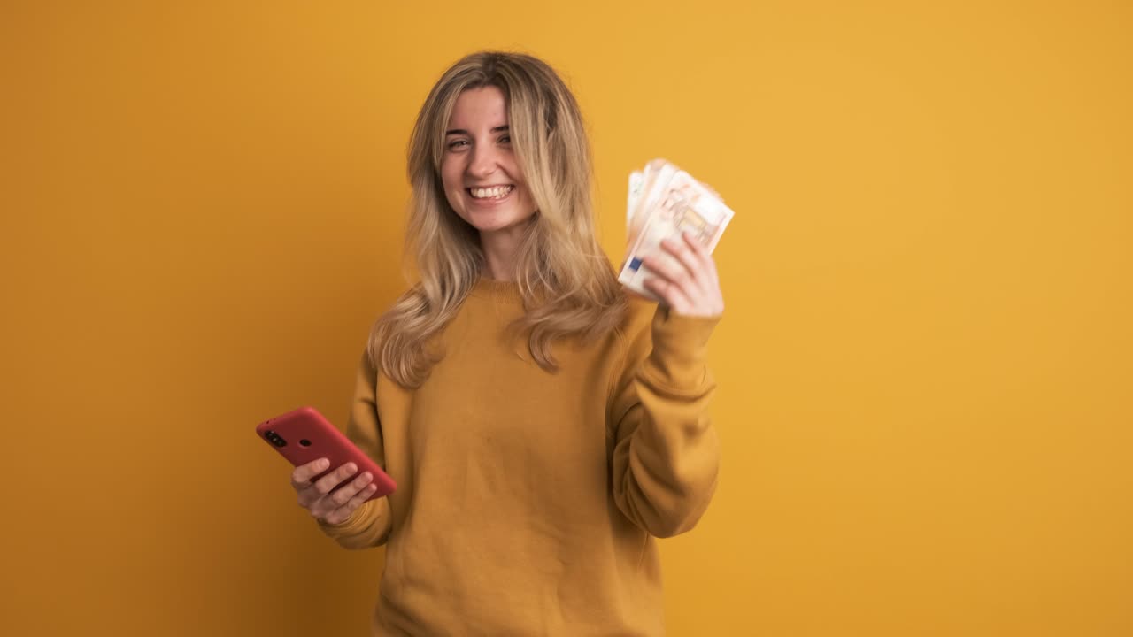Donna con smartphone e contanti che celebra un'impresa commerciale di successo su sfondo giallo.
