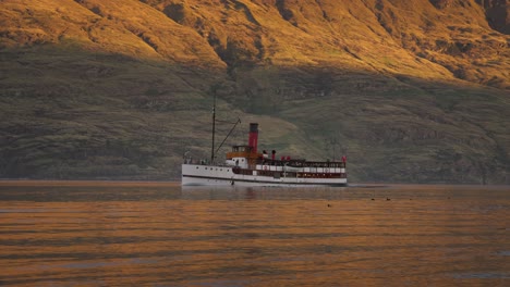 Old-steamboat-traveling-on-calm-alpine-lake-with-mountain-backdrop