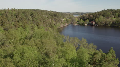 Vista-Inclinada-De-Drones-De-Una-Hermosa-Cabaña-Junto-A-Un-Lago-Forestal,-Suecia