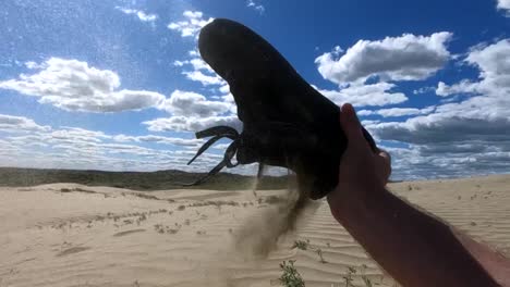 cámara lenta - la persona se quita el zapato en el desierto y vacía la arena del zapato